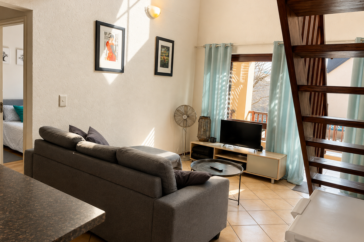 A bright living room featuring tiled flooring, a wooden staircase leading to an upper level, and direct access to an outdoor balcony area.