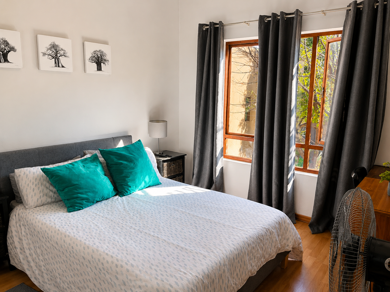 A bright and well-maintained bedroom featuring warm wooden flooring and large timber-framed windows with floor-to-ceiling curtains.