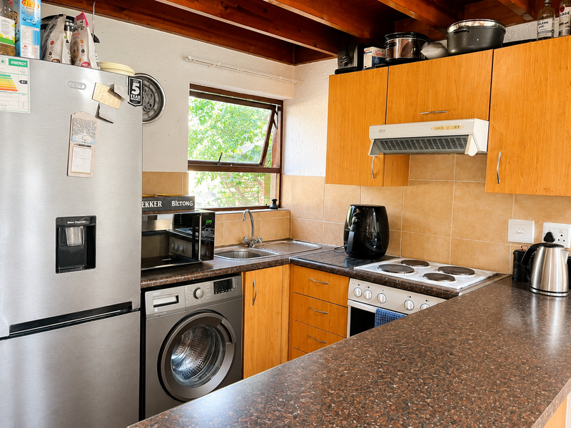 Functional kitchen featuring timber cabinetry, laminate countertops, tiled backsplash, built-in oven, hob, extractor fan, and exposed timber ceiling beams.