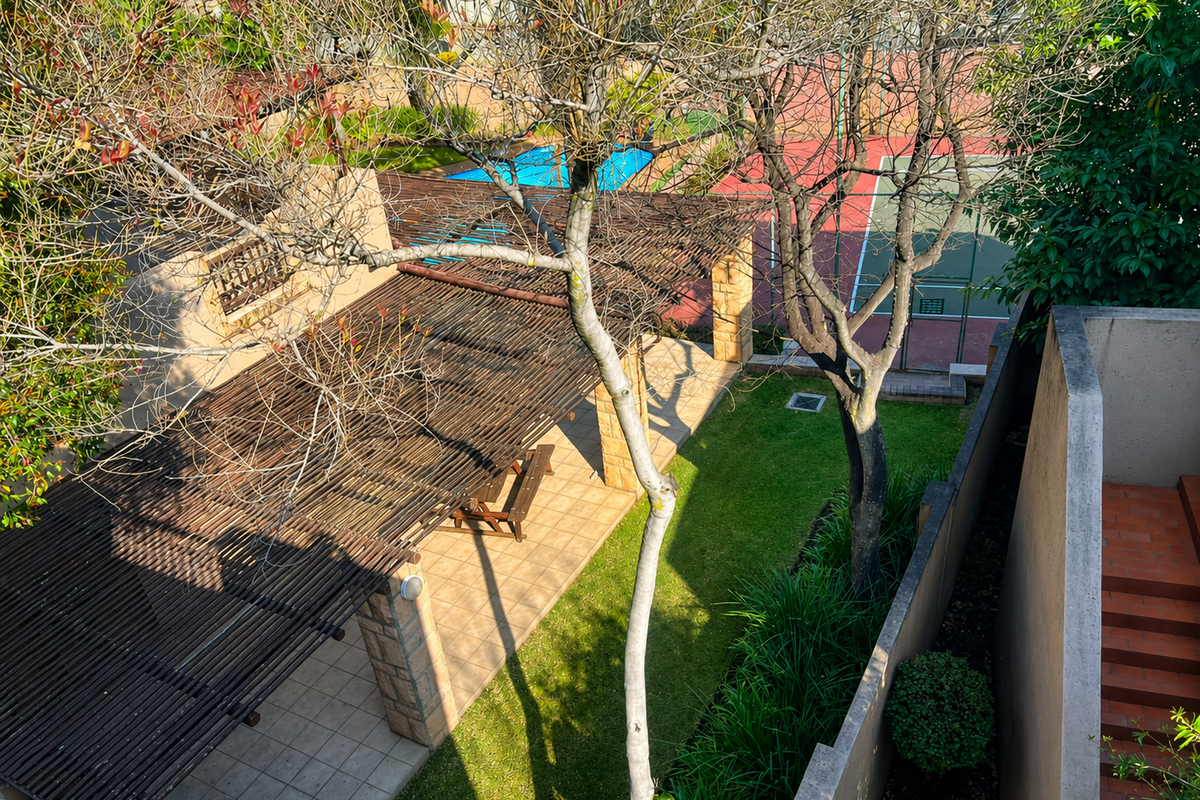 Aerial view of a residential complex featuring a covered patio with a pergola, a swimming pool, and a private tennis court.