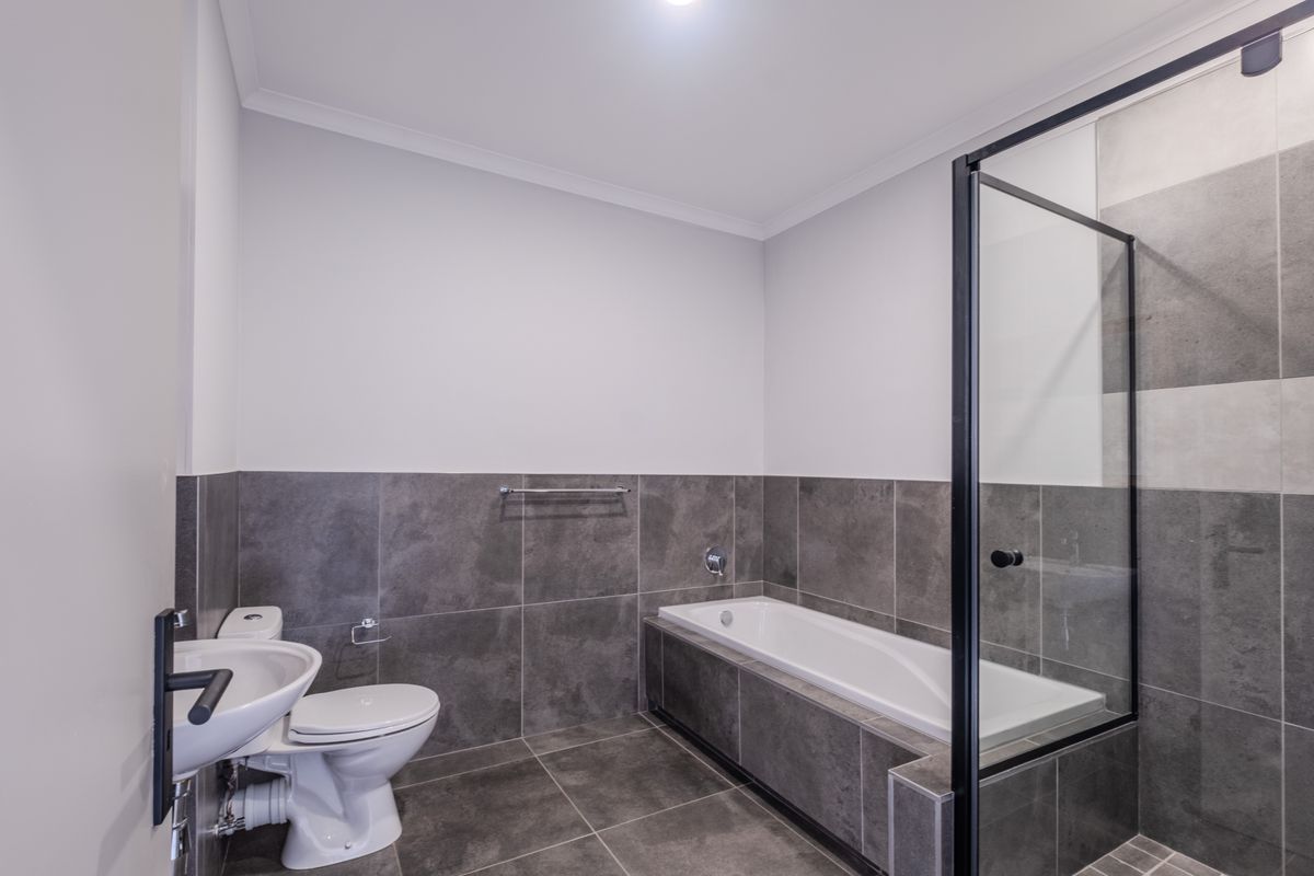 Modern bathroom featuring a built-in bathtub, separate glass-enclosed shower, wall-mounted basin, and contemporary grey floor-to-wall tiling.
