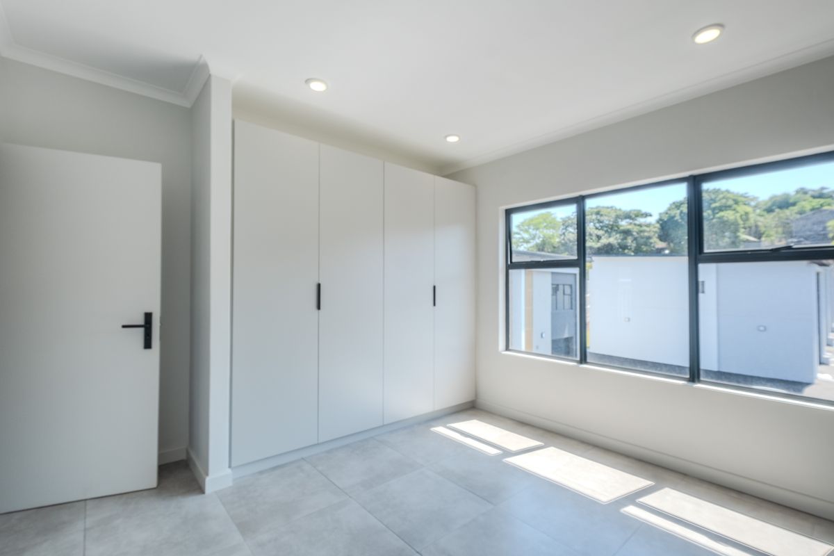 A bright, modern bedroom featuring neutral tiled flooring, built-in cupboards, and large windows that provide ample natural light.
