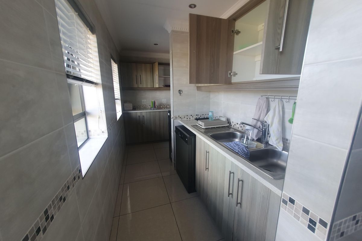 A functional galley-style kitchen featuring wood-look cabinetry, tiled walls, and a double stainless steel sink with integrated plumbing.