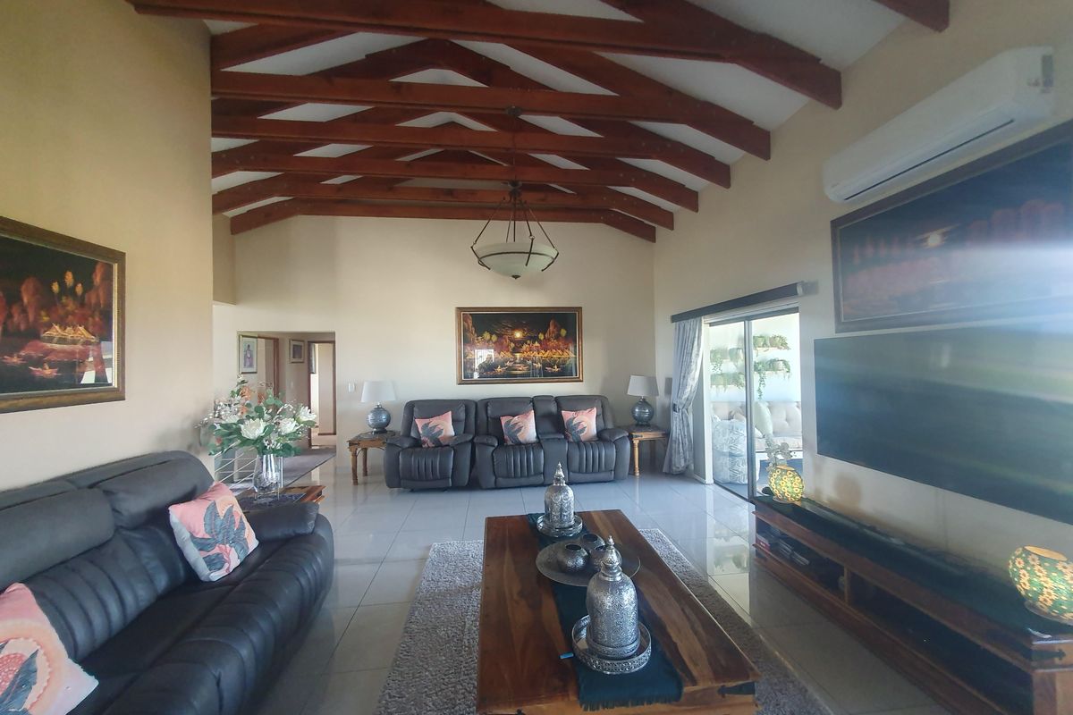 Spacious living room featuring high vaulted ceilings with exposed timber beams, tiled flooring, and a wall-mounted air conditioning unit.