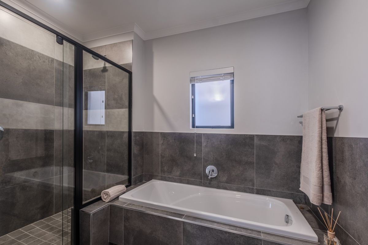 Modern bathroom featuring a built-in bathtub, a separate walk-in shower with black-framed glass, and contemporary grey tiling throughout.