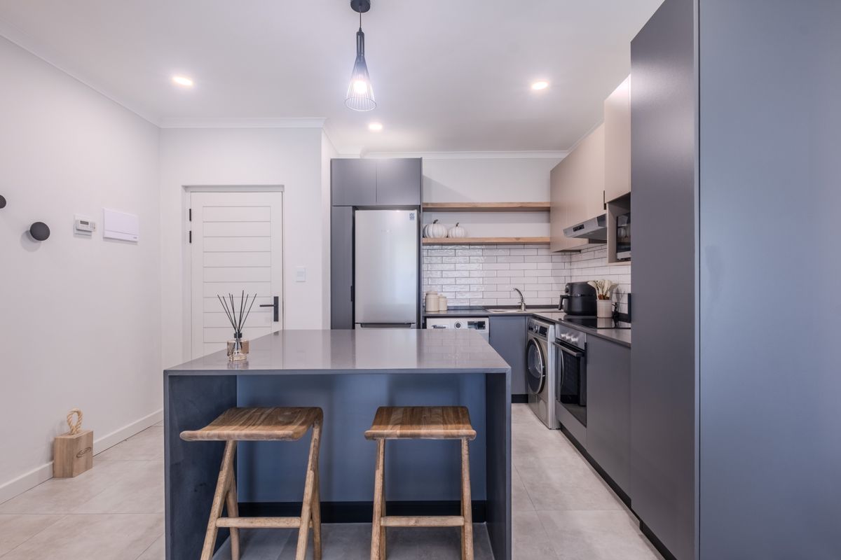 Modern kitchen featuring sleek grey cabinetry, a central island, subway tile backsplash, floating timber shelving, and integrated appliances.