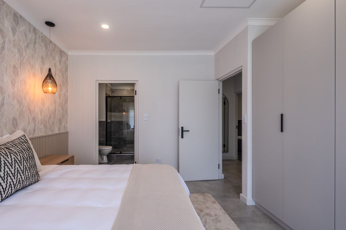 Modern bedroom featuring built-in wardrobes, feature wallpaper, pendant lighting, and an adjoining en-suite bathroom with tiled flooring throughout.