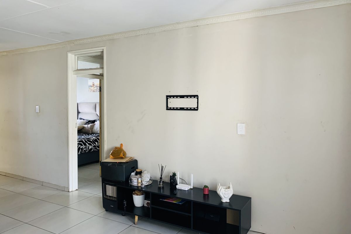 A living room area featuring tiled flooring, decorative ceiling cornicing, and a wall-mounted TV bracket, showing signs of wear on the wall surfaces.
