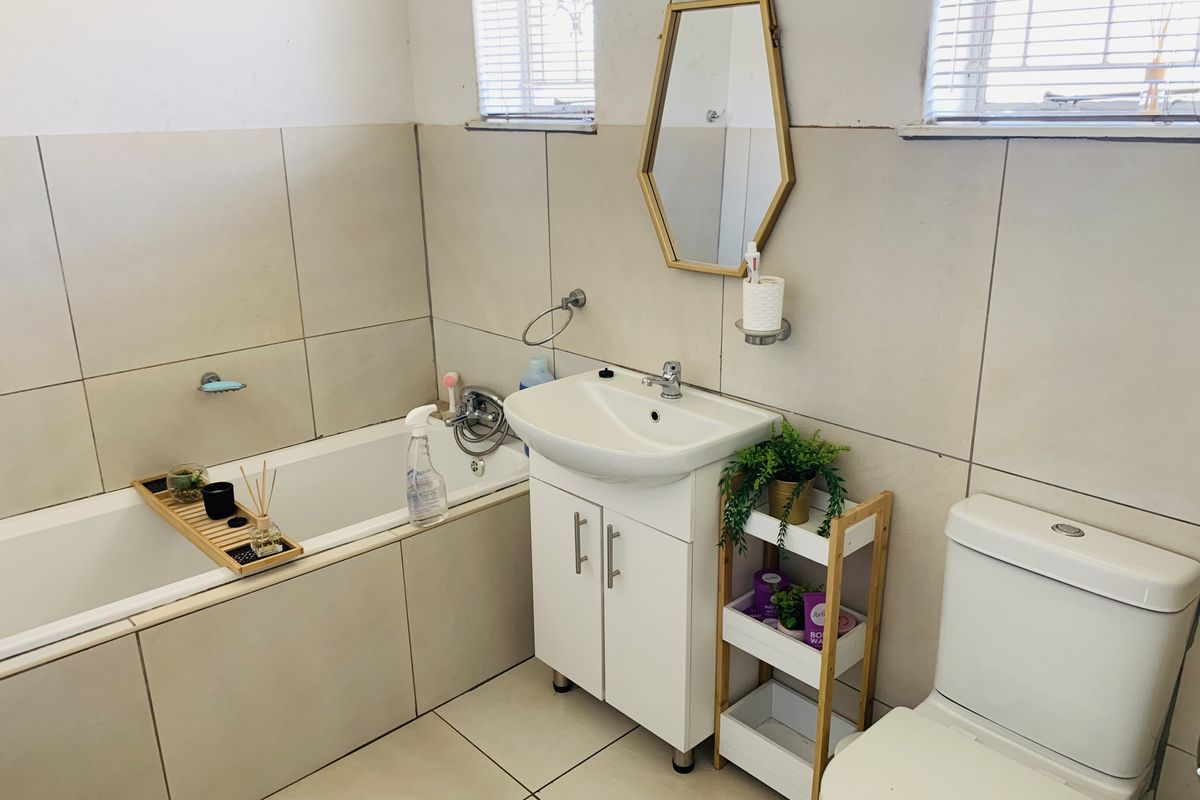 A functional bathroom featuring a built-in bathtub, vanity cabinet with basin, and a standard toilet, finished with neutral wall and floor tiles.