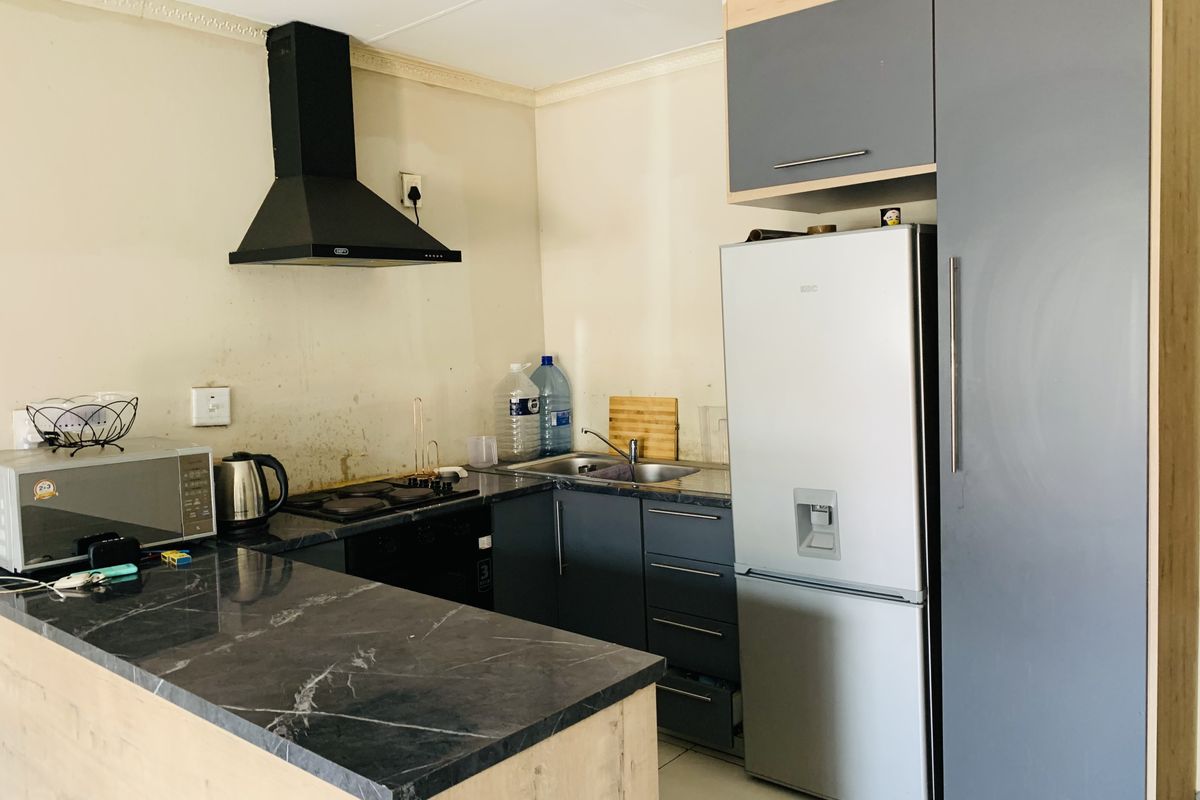 A compact kitchen featuring dark cabinetry, stone countertops, a built-in hob, and an extractor fan, with tiled flooring throughout.