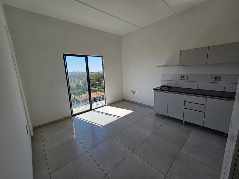 An open-plan living and kitchen area featuring tiled floors, modern cabinetry with a built-in hob, and a sliding door leading to a balcony.