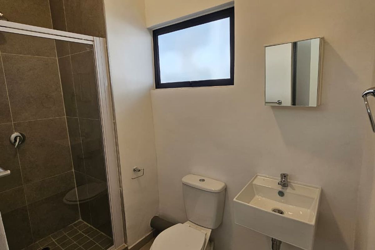 A compact bathroom featuring a shower enclosure, wall-mounted basin, and toilet, with tiled flooring and neutral wall finishes.