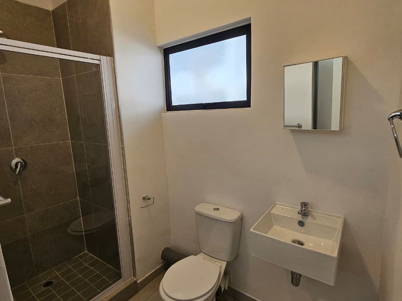 A compact bathroom featuring a shower enclosure, wall-mounted basin, and toilet, with tiled flooring and neutral wall finishes.