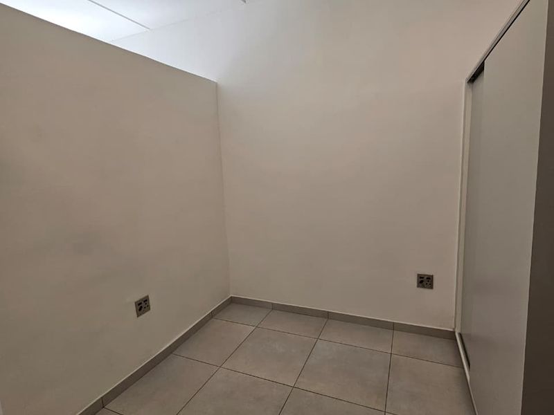 A clean, empty bedroom featuring neutral tiled flooring and a built-in wardrobe, providing a versatile space ready for personalization.