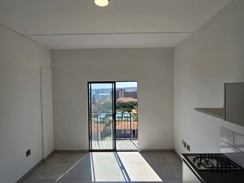 Bright open-plan living area featuring tiled floors, a modern kitchen with gas hob, and a sliding door leading to a balcony with views.