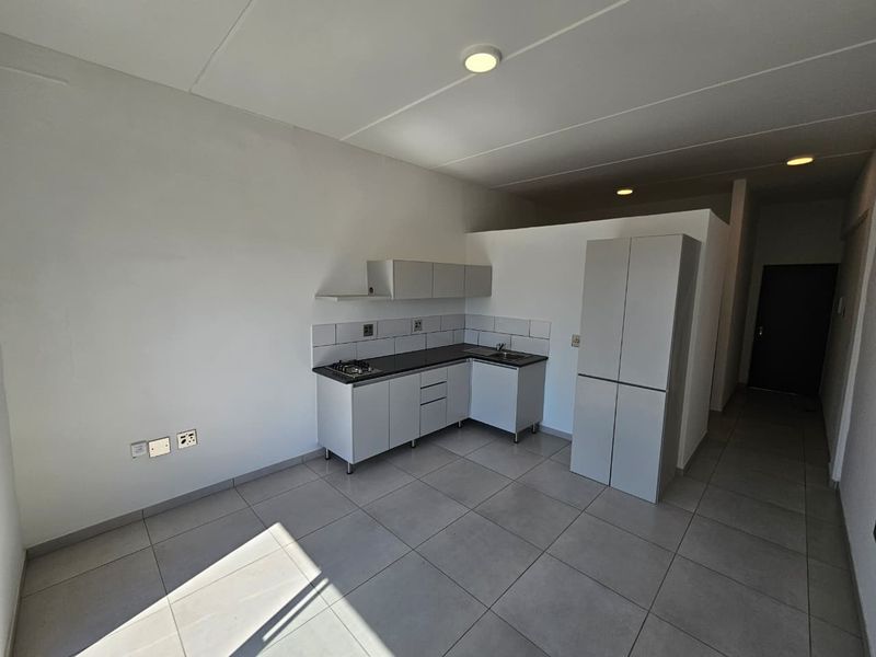 A clean, modern kitchen area featuring built-in cabinetry, a gas hob, tiled backsplash, and neutral floor tiles in an open-plan layout.