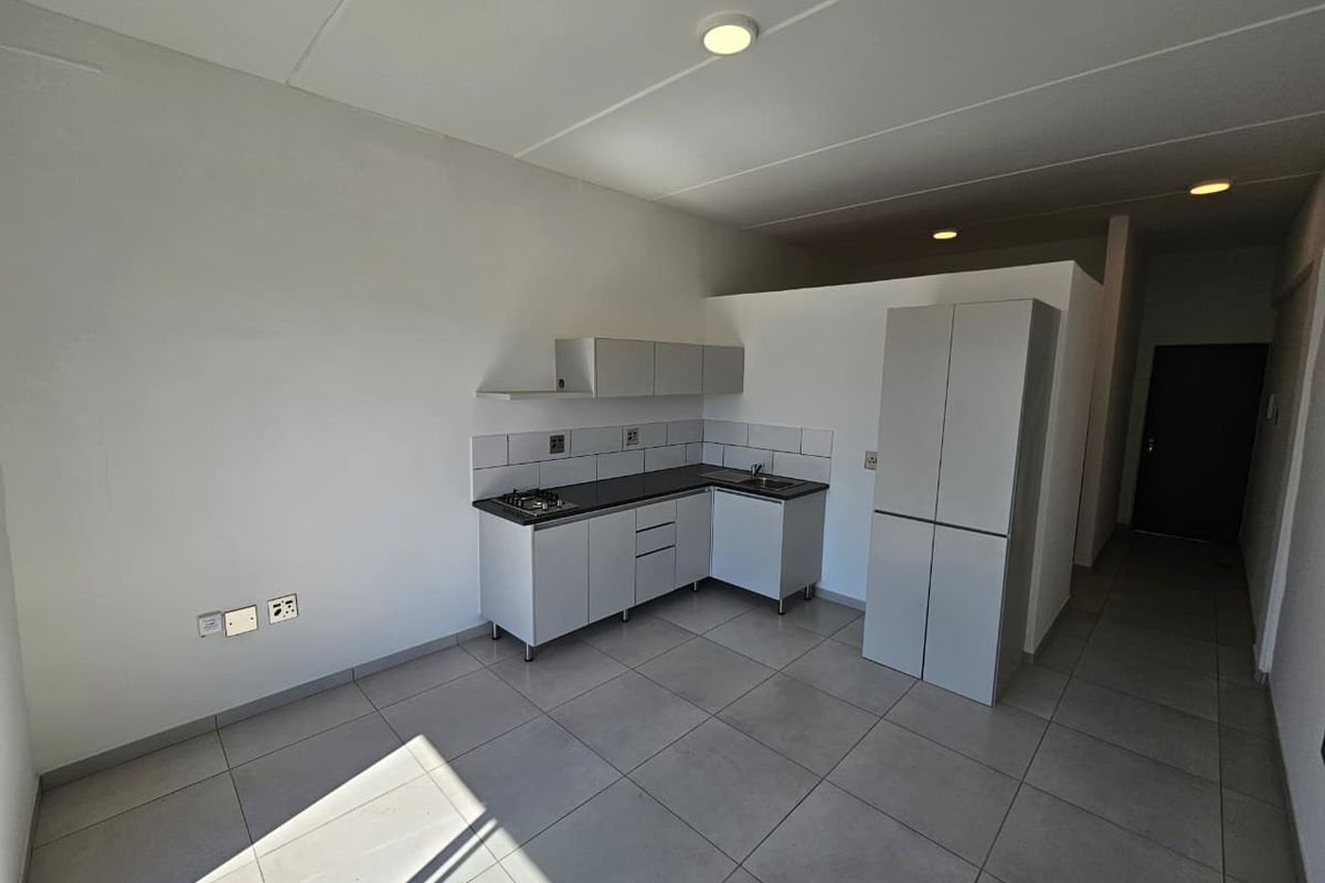 A clean, modern kitchen area featuring built-in cabinetry, a gas hob, tiled backsplash, and neutral floor tiles in an open-plan layout.