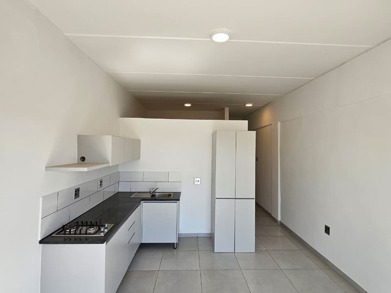 A clean, modern kitchen featuring white cabinetry, stone countertops, a gas hob, and neutral tiled flooring in an open-plan layout.
