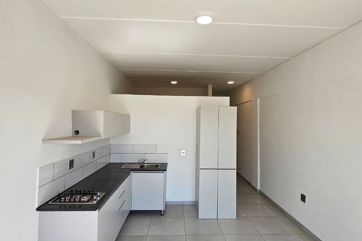 A clean, modern kitchen featuring white cabinetry, stone countertops, a gas hob, and neutral tiled flooring in an open-plan layout.