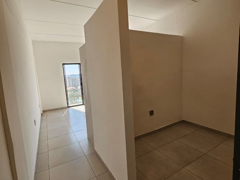 An empty bedroom featuring neutral tiled flooring and a central partition wall, providing a versatile layout with natural light from the adjacent balcony door.