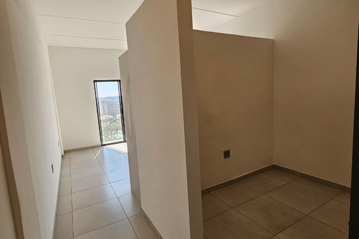 An empty bedroom featuring neutral tiled flooring and a central partition wall, providing a versatile layout with natural light from the adjacent balcony door.