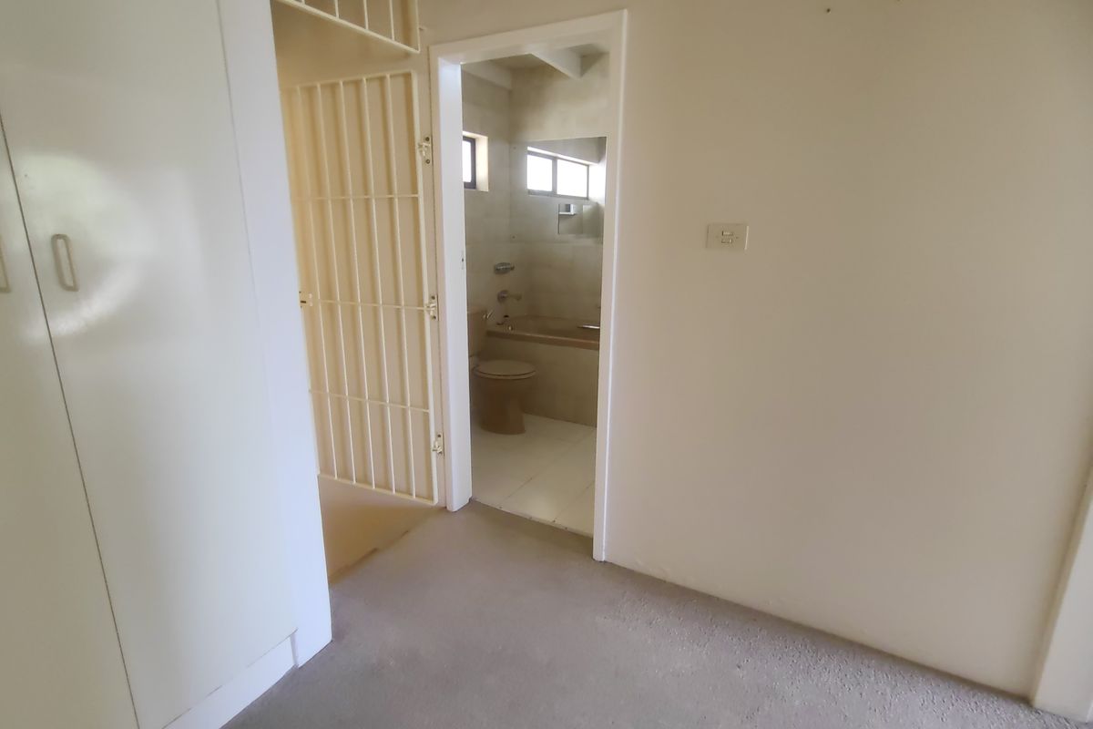 An empty bedroom featuring built-in cupboards and a security gate, with an adjoining bathroom visible through the doorway.