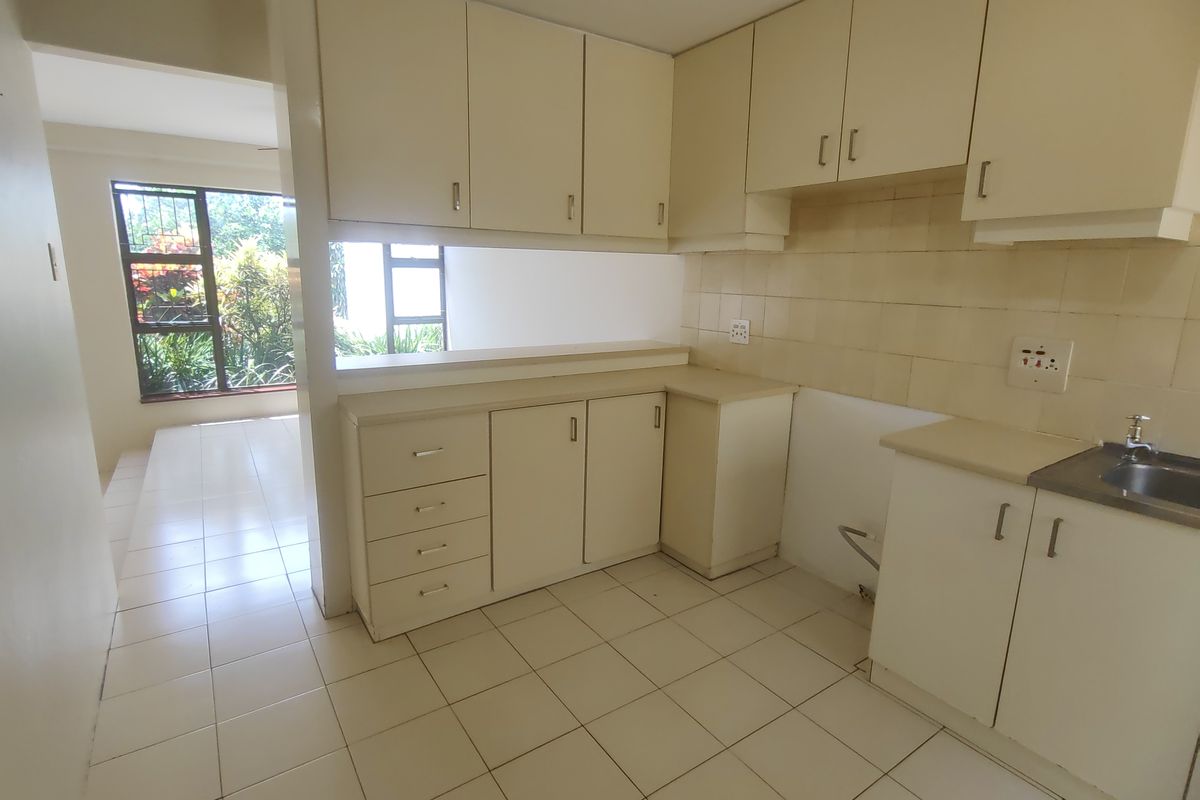 A functional, empty kitchen featuring laminate cabinetry, tiled backsplash, and a convenient pass-through window overlooking the adjacent living area.