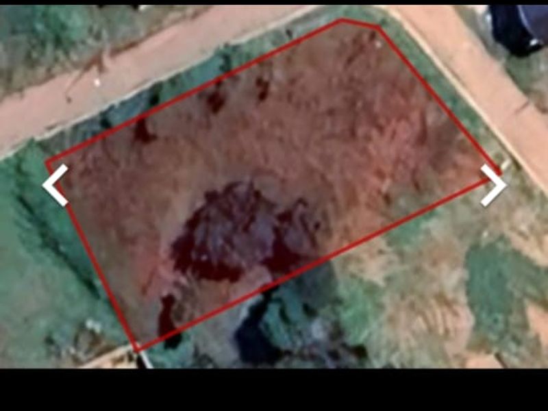 An aerial view of a vacant residential plot of land with boundary markers indicated.