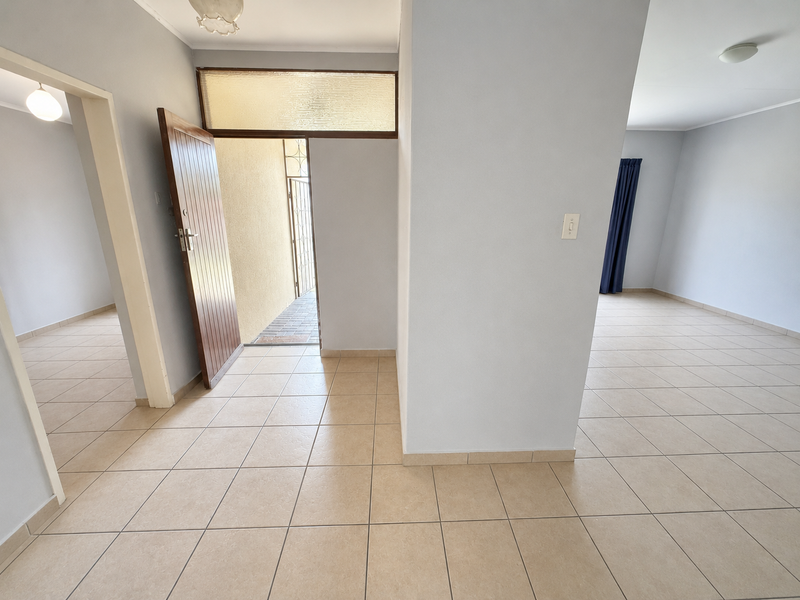 A bright and spacious entrance hall featuring neutral ceramic floor tiles and a timber front door with a transom window.