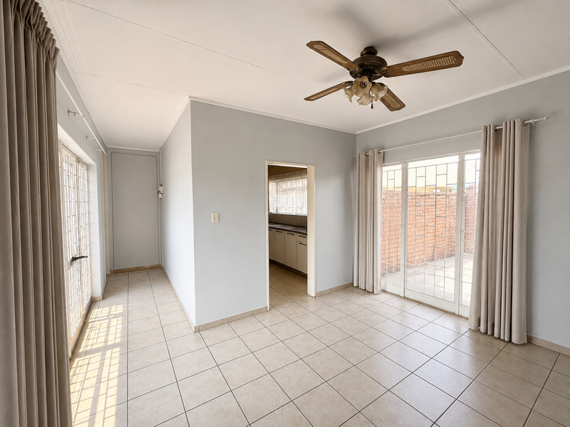 Bright and spacious living area featuring neutral ceramic floor tiles, a ceiling fan, and sliding glass doors providing access to the outdoor space.