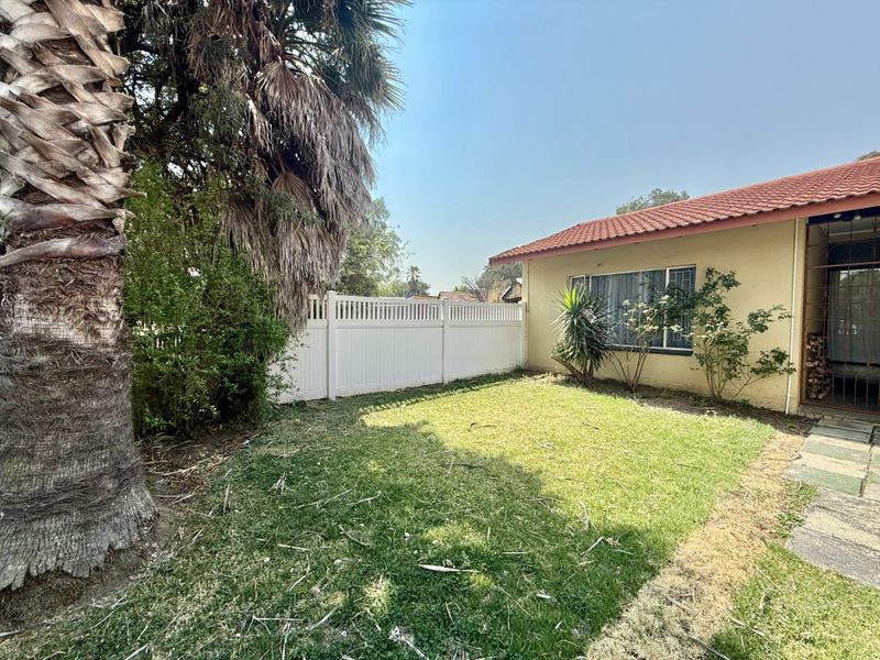 A private rear garden area featuring a lawn, paved walkway, and white vinyl fencing, adjacent to the townhouse exterior with a tiled roof.