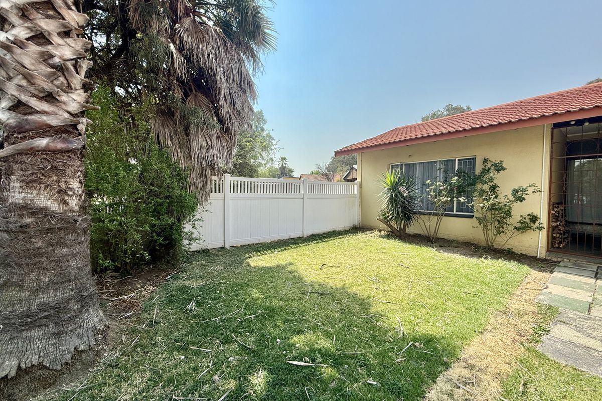 A private rear garden area featuring a lawn, paved walkway, and white vinyl fencing, adjacent to the townhouse exterior with a tiled roof.