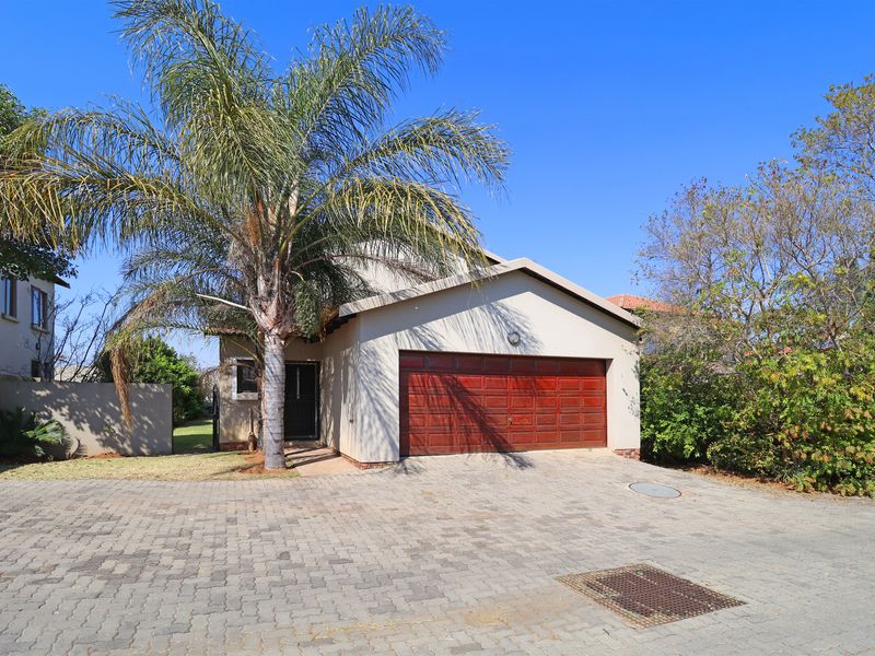 Front exterior view of the townhouse featuring a paved driveway, a double garage with a timber door, and established garden surroundings.