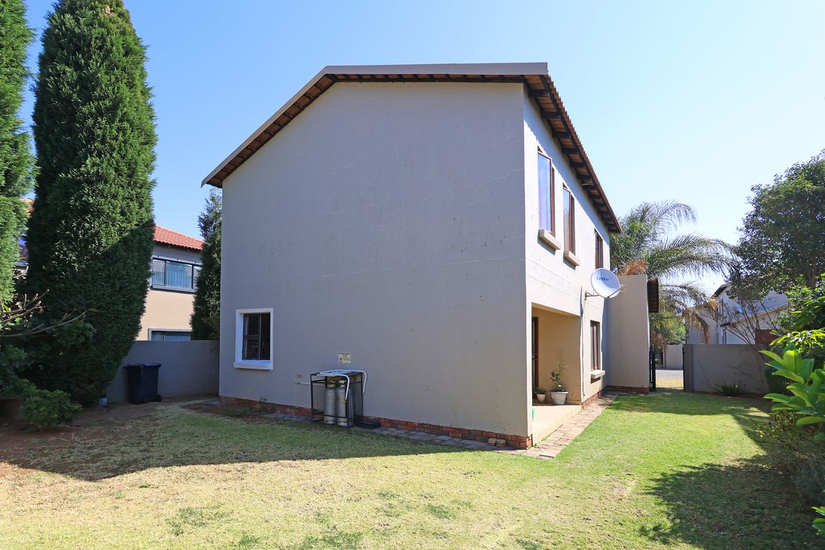 Rear view of the townhouse featuring a private garden, paved walkway, and exterior wall with a mounted satellite dish.