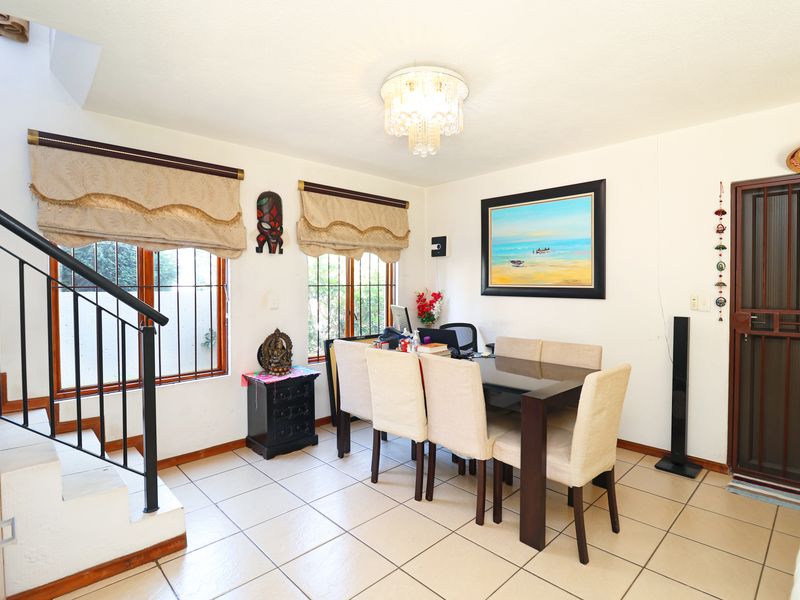 Dining area featuring ceramic tile flooring, a central crystal chandelier, and a staircase with a metal railing, providing access to the upper level.