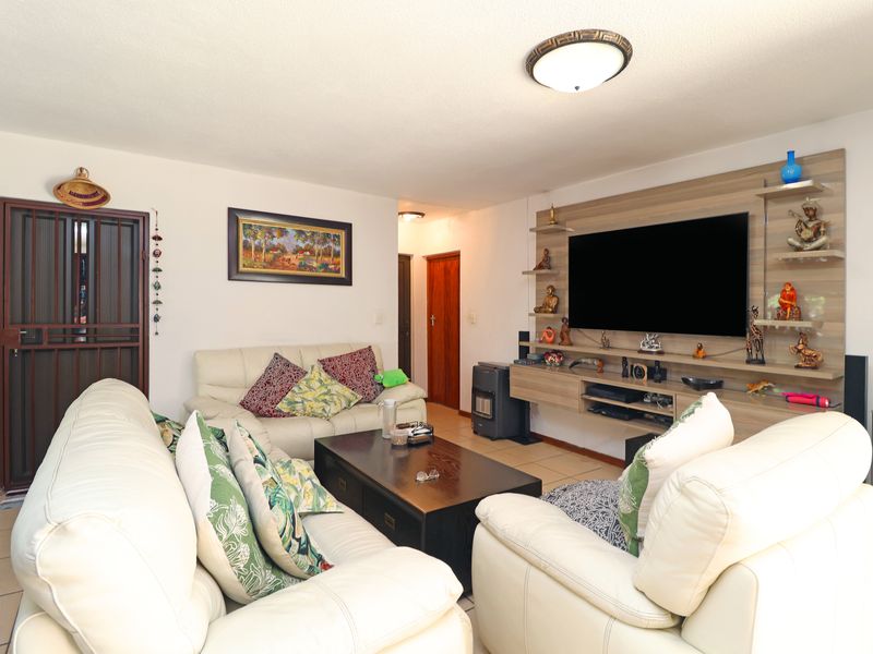 A comfortable living room featuring tiled flooring, a built-in media wall unit, and a secure entrance gate.