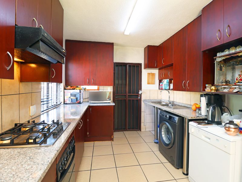 Functional kitchen featuring dark wood cabinetry, granite countertops, gas hob, extractor fan, and tiled flooring with direct access to a secure rear entrance.