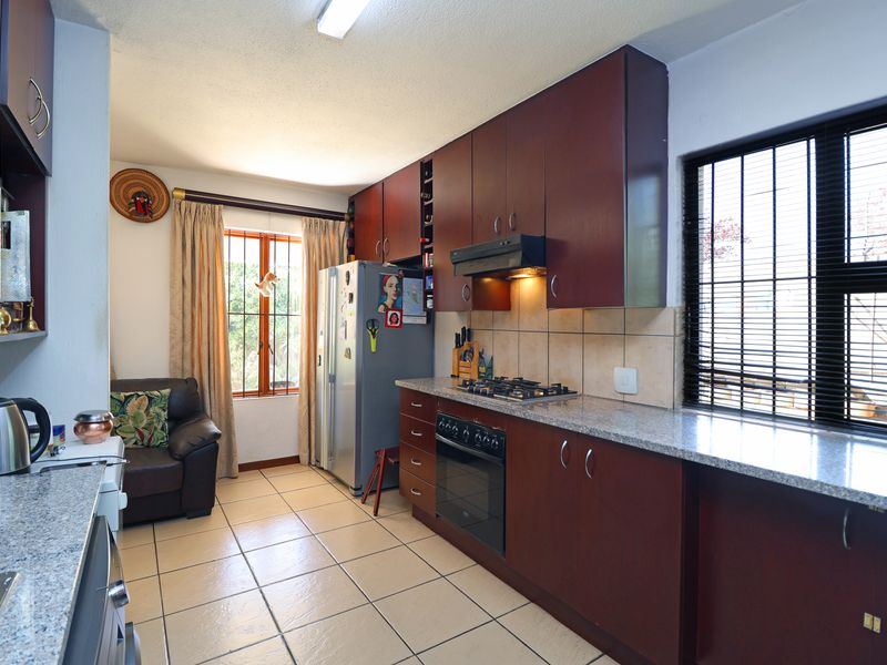 A functional kitchen featuring dark wood cabinetry, granite countertops, a gas hob, and built-in oven, complemented by tiled flooring and natural light.