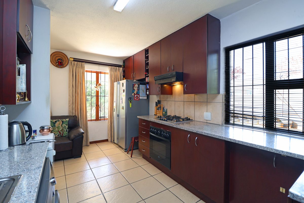 A functional kitchen featuring dark wood cabinetry, granite countertops, a gas hob, and built-in oven, complemented by tiled flooring and natural light.