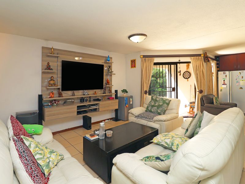 A comfortable living room featuring a modern built-in media unit, ceramic tiled flooring, and direct access to an outdoor patio area through sliding doors.