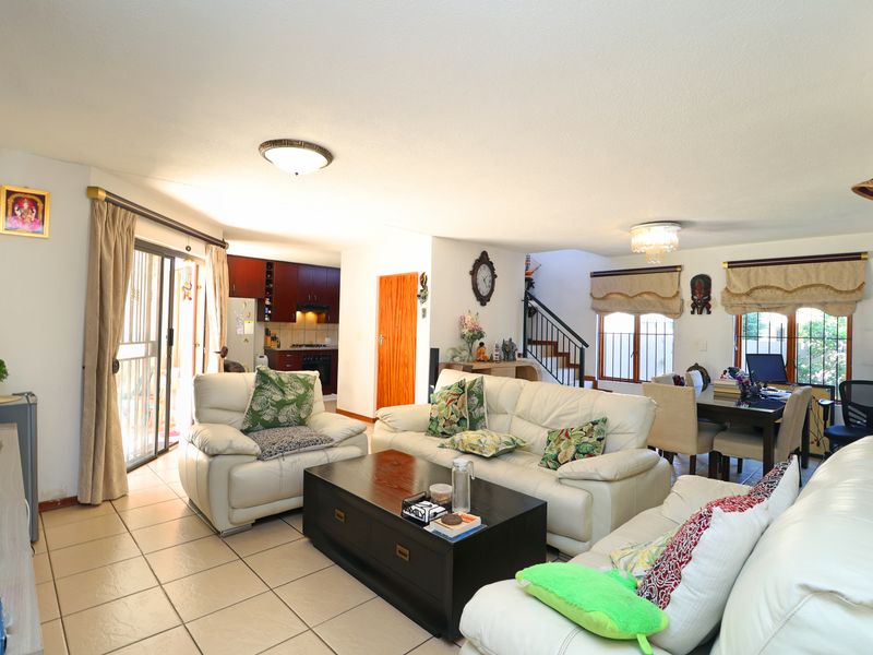Spacious open-plan living and dining area featuring ceramic tiled flooring, a staircase with metal railing, and an integrated kitchen with built-in cabinetry.