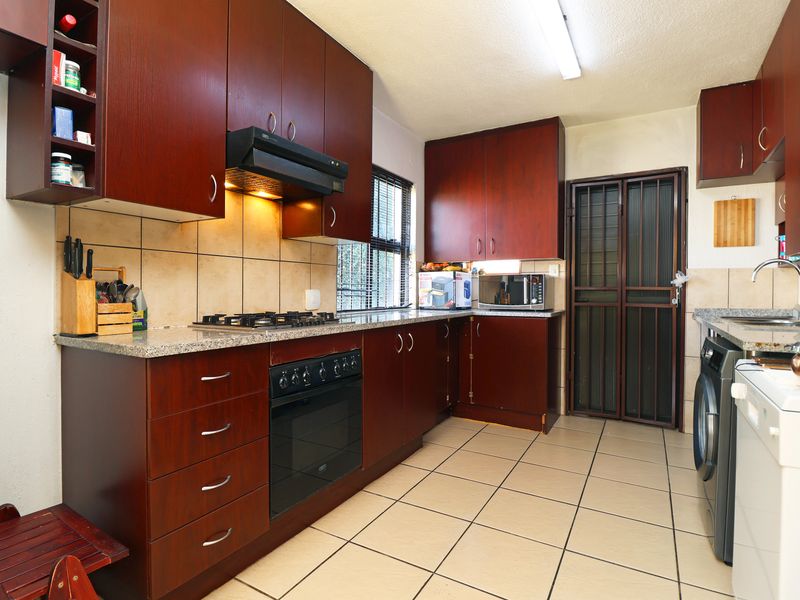 Functional kitchen featuring dark wood cabinetry, granite countertops, gas hob, built-in oven, and tiled flooring with direct access to an exterior security gate.