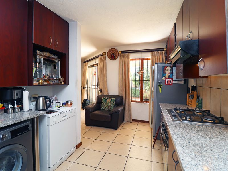 Functional kitchen featuring dark wood cabinetry, granite countertops, and a gas hob, with an adjacent living area and tiled flooring throughout.