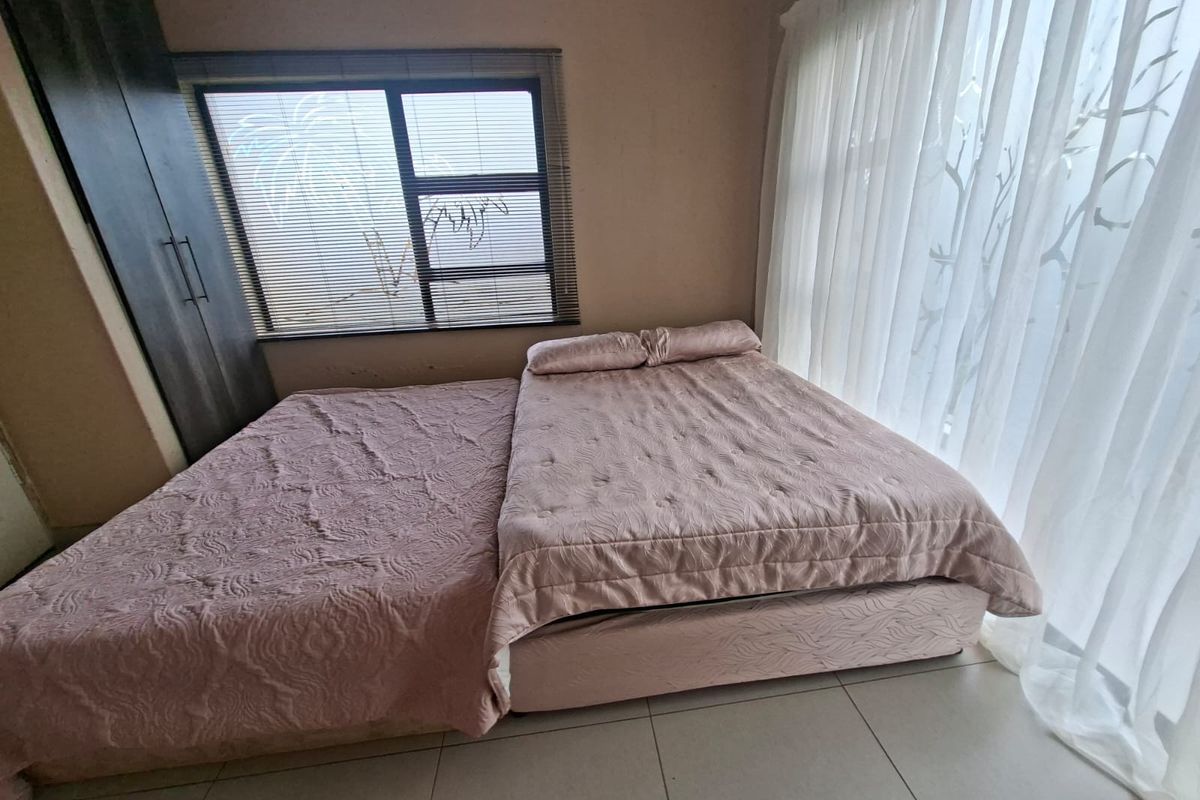A bedroom featuring built-in cupboards, tiled flooring, and large windows with blinds and curtains, providing natural light.