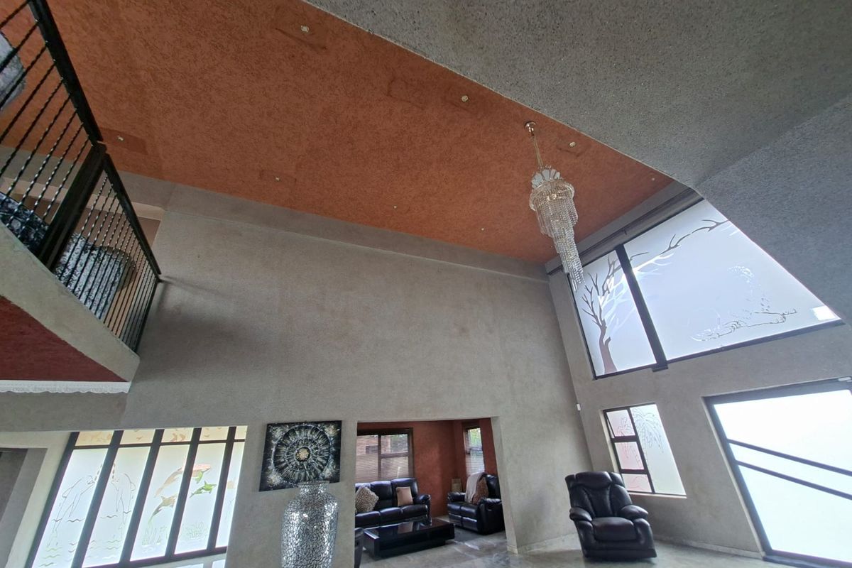 Spacious double-volume living area featuring high ceilings, a decorative chandelier, large windows with frosted glass detailing, and a mezzanine level with a metal balustrade.