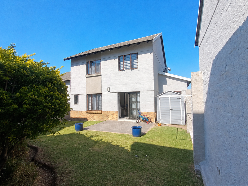 Rear view of the townhouse featuring a private garden, paved patio area, and secure sliding door access to the main living space.