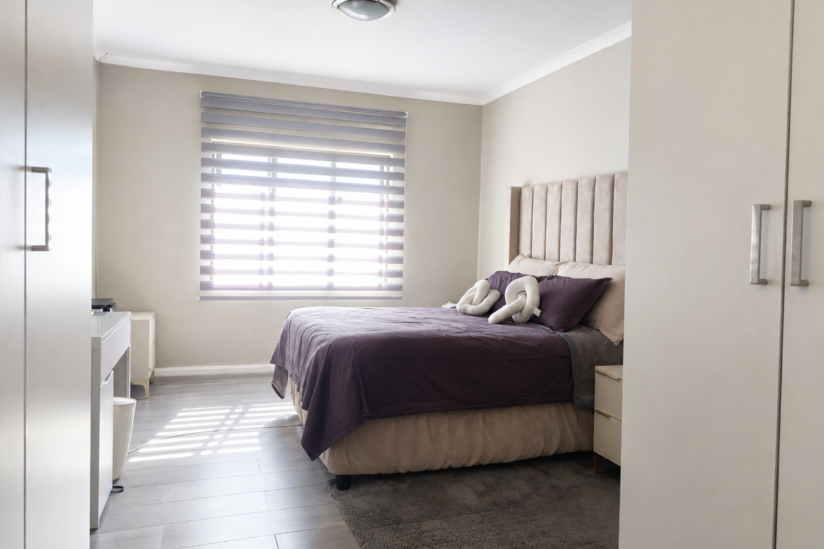 A well-maintained bedroom featuring neutral wall tones, tiled flooring, built-in cupboards, and modern roller blinds for adjustable natural light.