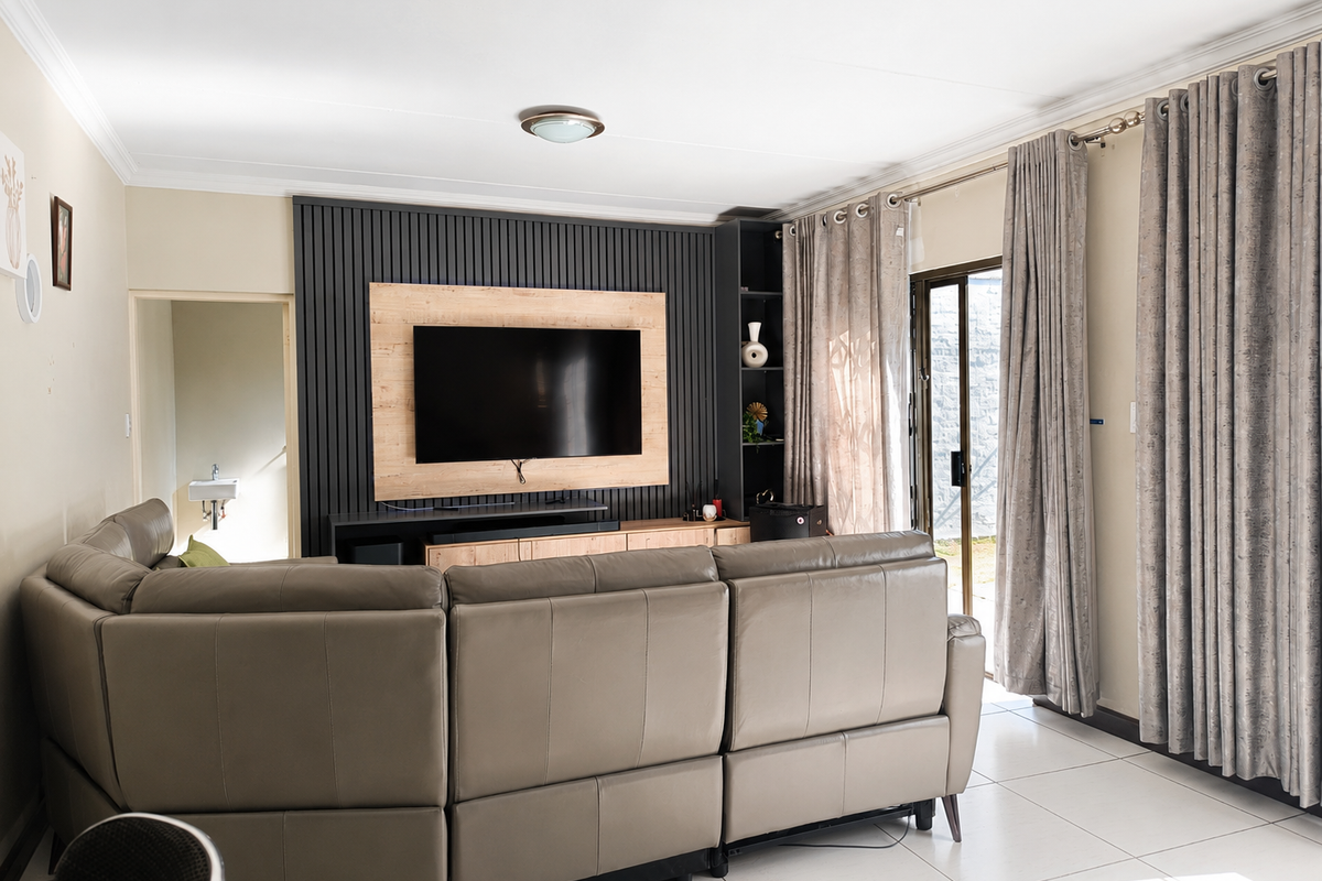 A well-maintained living room featuring a modern built-in media wall with slatted paneling, tiled flooring, and direct access to an outdoor area.