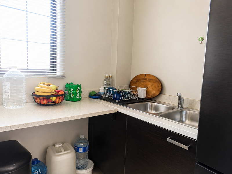 A functional scullery area featuring dark wood-grain cabinetry, a double stainless steel sink with mixer tap, and stone-look countertops.