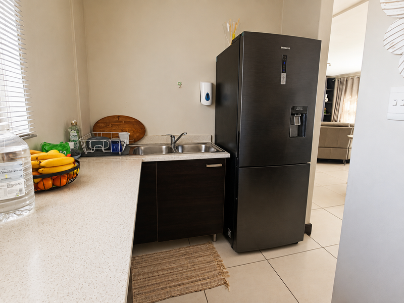 A functional scullery area featuring a double bowl sink, stone countertops, dark wood cabinetry, and tiled flooring, providing additional prep and wash-up space.